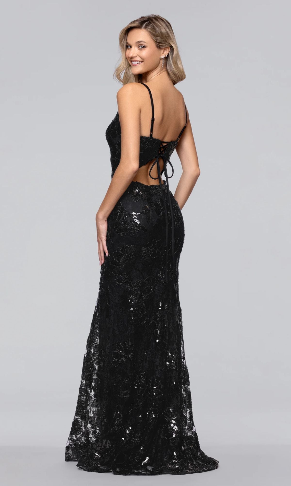 Model wearing the Long Sequin-Print Prom Dress: Blondie Nites 5883BN, a black, floor-length gown with thin straps and an open lace-up back, stands smiling over her shoulder.